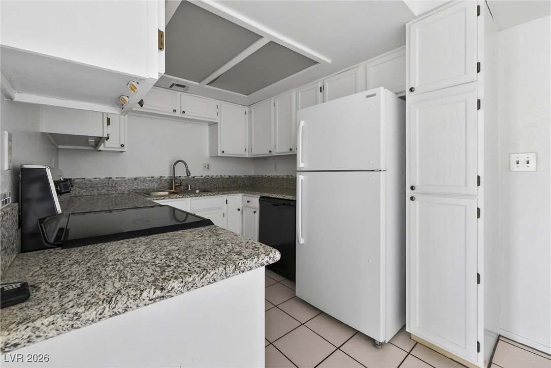 Kitchen with white cabinets, granite counters, tiled floor, and a white refrigerator.