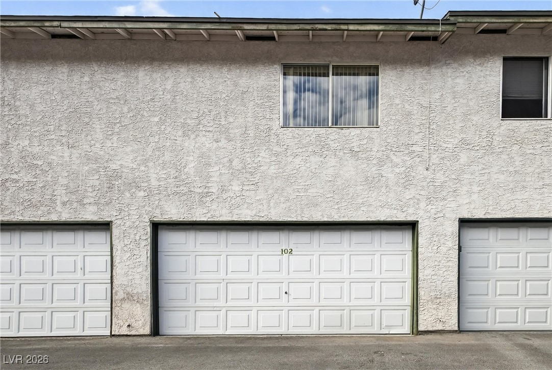 Building exterior with unit 102’s white garage door beneath a second-story window.