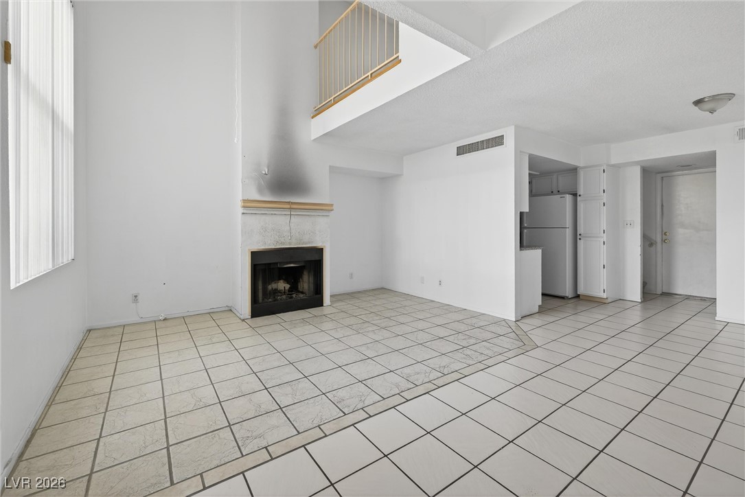 Vacant living room with tiled floors, a fireplace, and open loft railing.