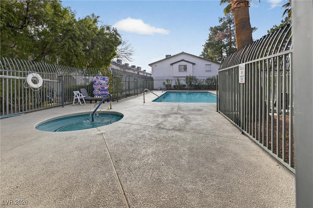 Community pool and circular spa behind metal fencing, with concrete decking and a life ring.