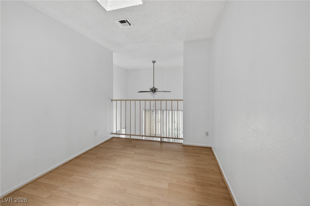Vacant upstairs room with wood-look flooring, ceiling fan, and railing overlooking a lower level.