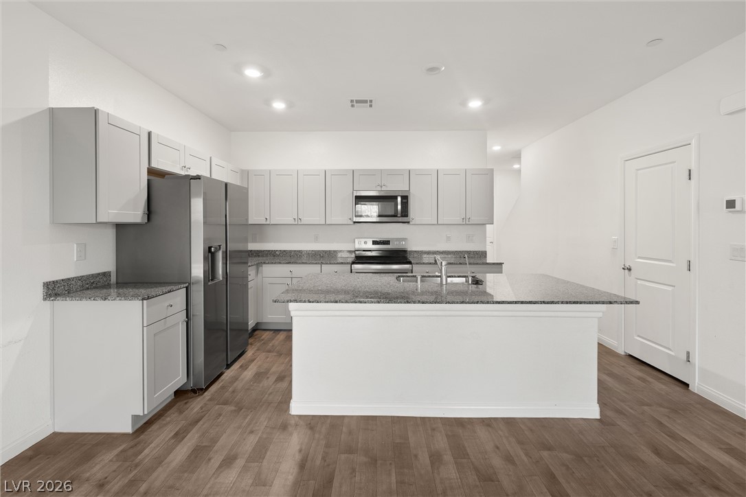Bright kitchen with white cabinetry, granite island, stainless steel appliances, and wood-look flooring.