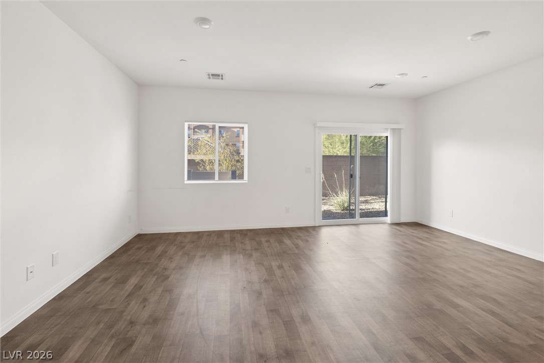 Vacant living room with wood-look flooring, a window, and sliding glass doors to the patio.