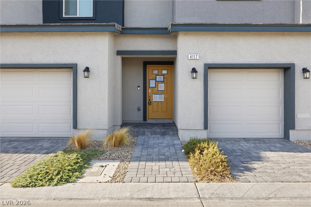 Home exterior with a recessed wooden entry between two garage doors and a paver walkway.