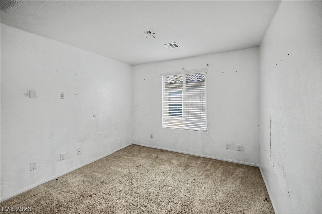 Empty carpeted room with window blinds and marked white walls.