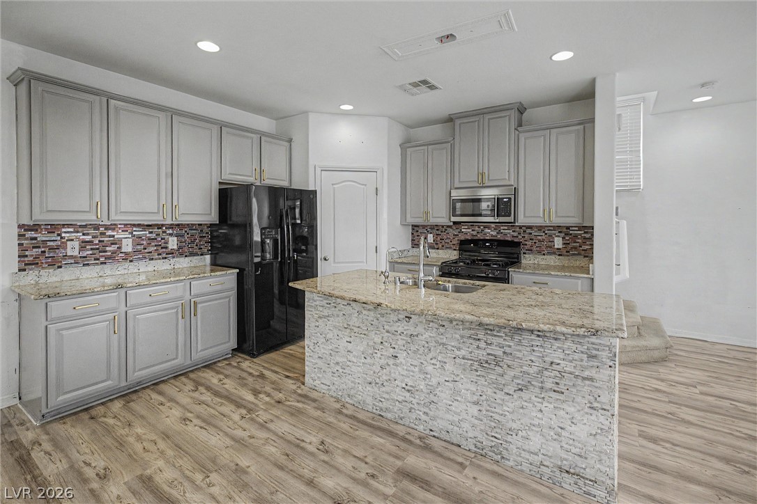 Kitchen with a large stone-topped island, gray cabinets, black appliances, and mosaic tile backsplash.