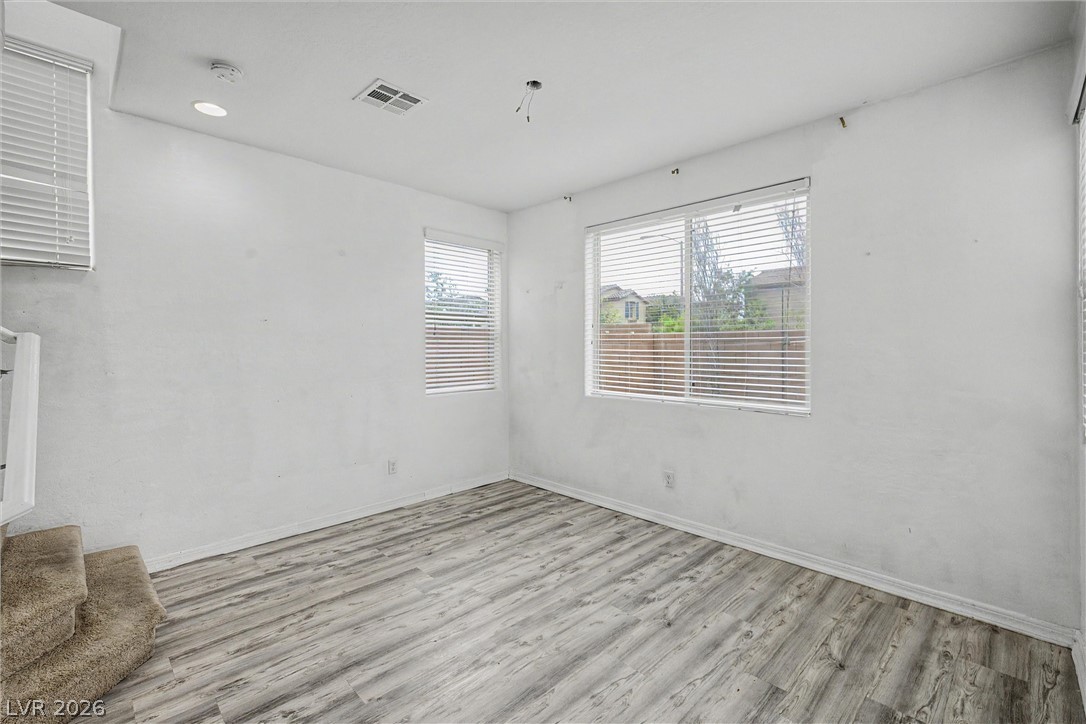 Empty room with gray wood-look flooring, white walls, and windows with blinds.