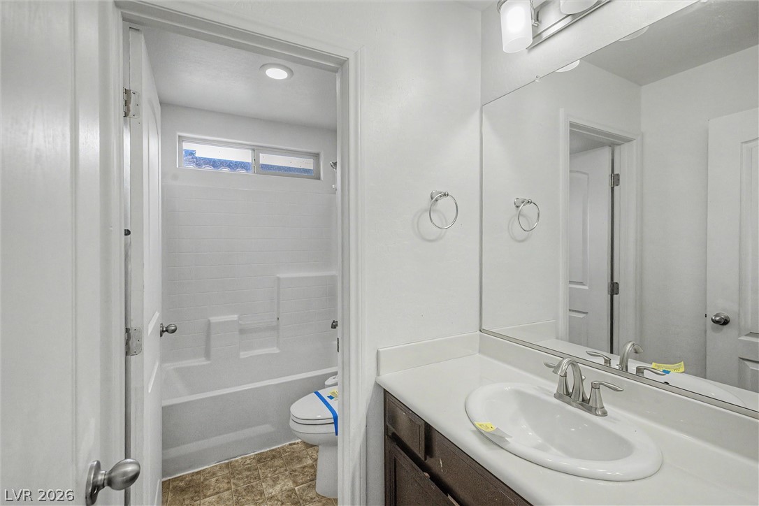 Bathroom with a white tub and high window beside a dark wood vanity and large mirror.