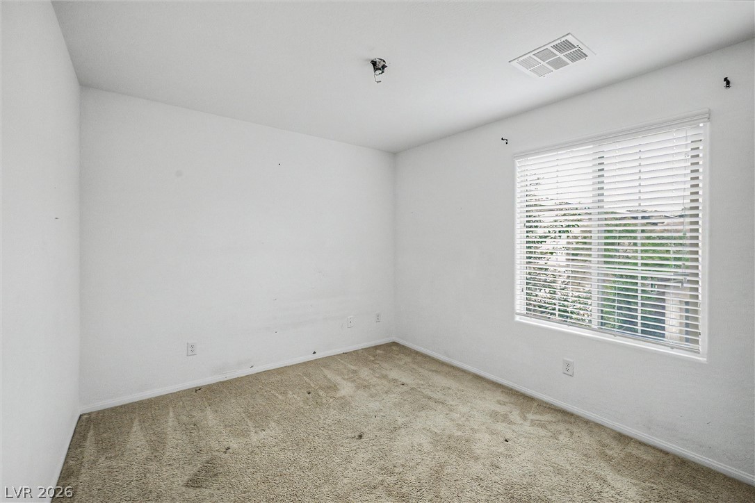Empty carpeted room with white walls and a large window fitted with blinds.