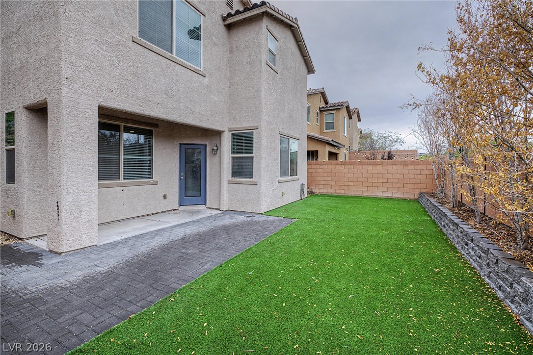 House backyard with artificial turf, a paver patio, and a stone-edged planting bed.