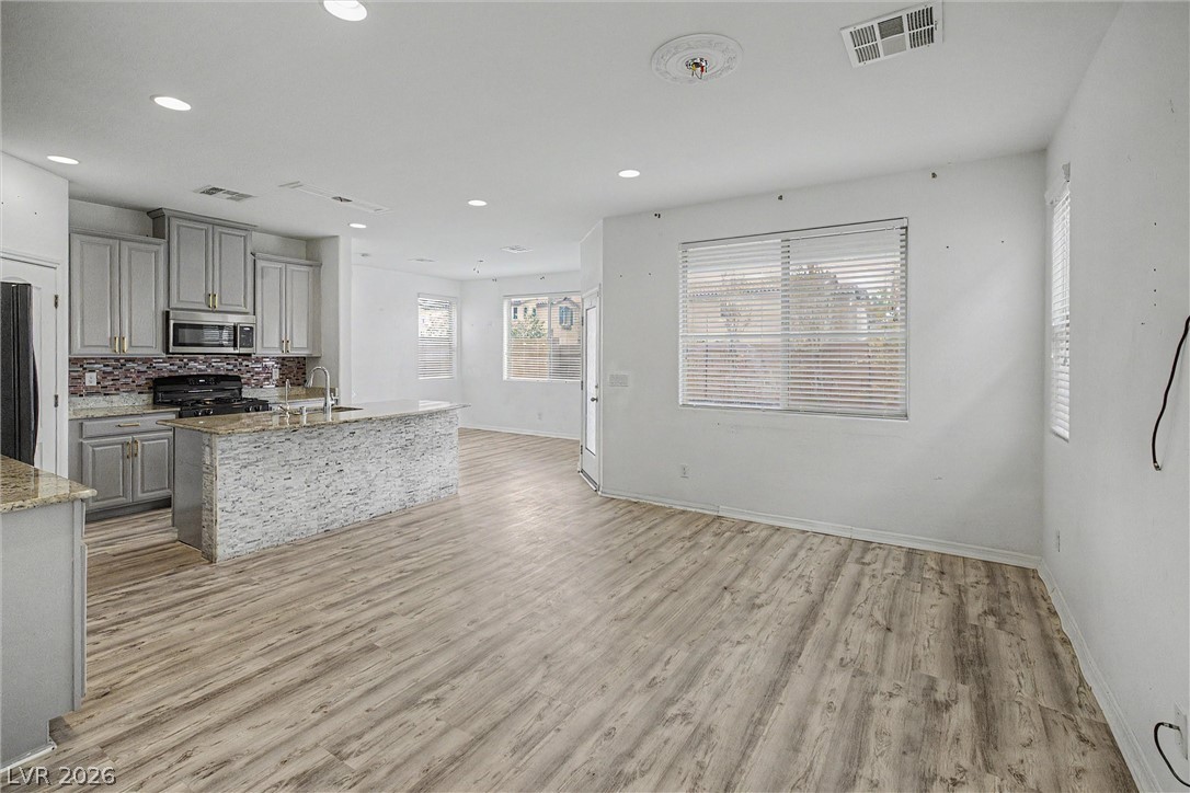 Open-plan kitchen with gray cabinets, a stone-faced island, and light wood-look flooring.
