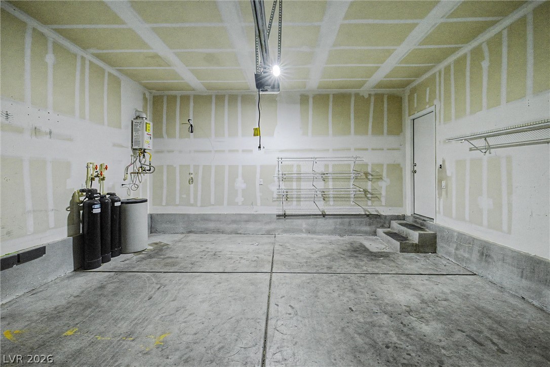 Empty garage with unfinished drywall, concrete floor, wire storage racks, and utility equipment.