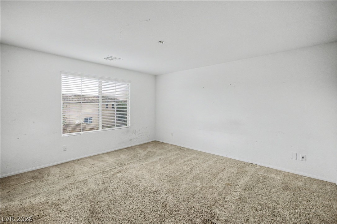 Empty carpeted room with white walls, a wide window, and horizontal blinds.