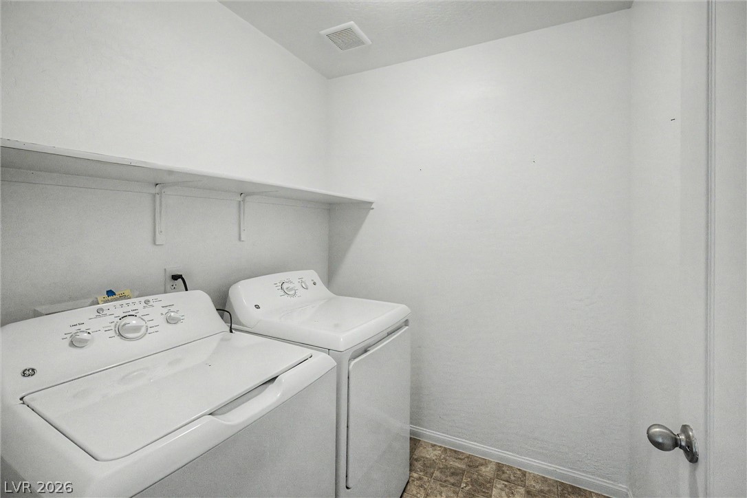 Laundry room with a white washer and dryer beneath a wall shelf.