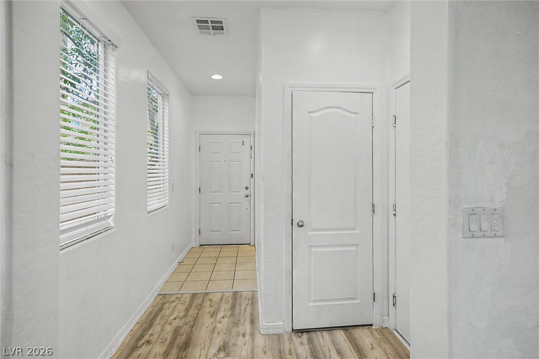 Vacant hallway with shuttered windows, wood-look flooring, and a tiled entry area.