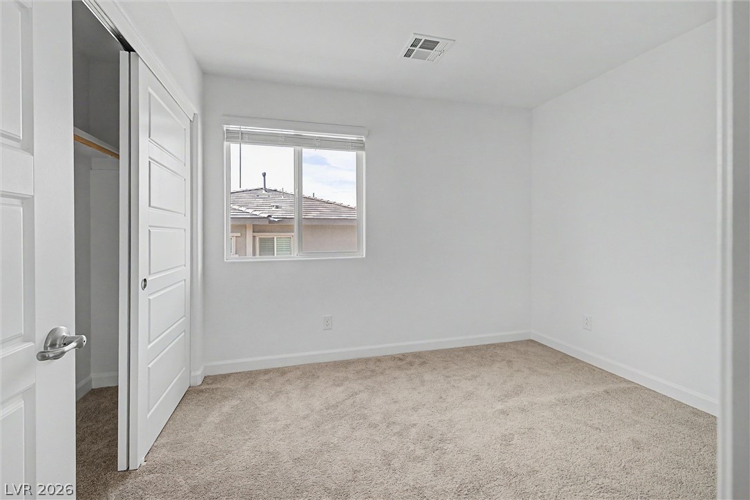 Unfurnished bedroom with beige carpet, a window with blinds, and an open paneled door.