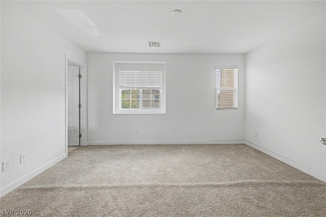 Empty carpeted bedroom with gray walls and two windows with blinds.