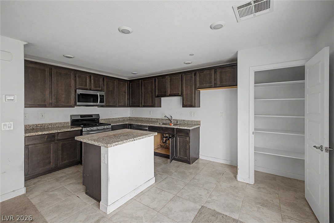 Kitchen with dark wood cabinets, granite countertops, a central island, and an open pantry.