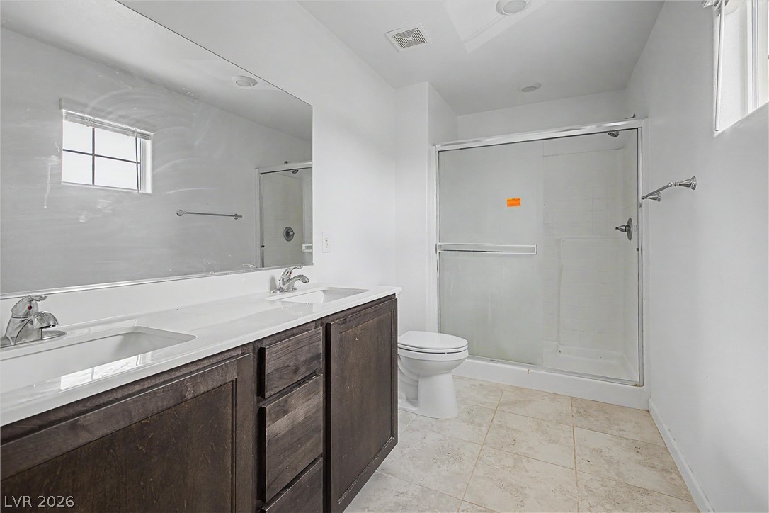 Bathroom with a dark double-sink vanity, large mirror, toilet, and glass-enclosed shower.