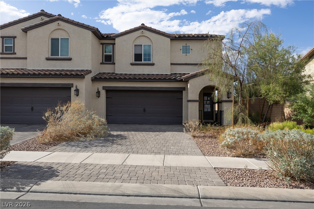 Two-story stucco home with two garages, a broad paver driveway, and desert landscaping.