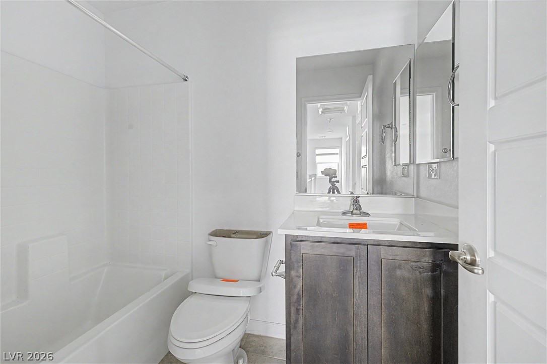 Bathroom with a white bathtub, toilet, and dark wood vanity beneath a wide mirror.