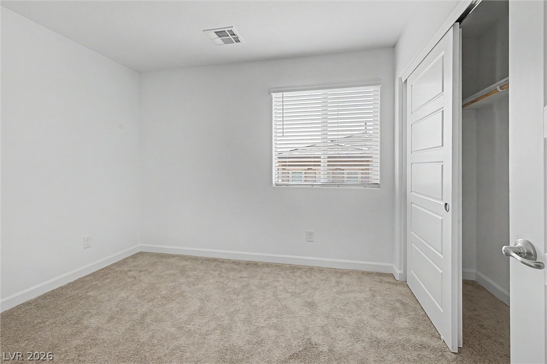 Vacant carpeted bedroom with window blinds and an open closet.