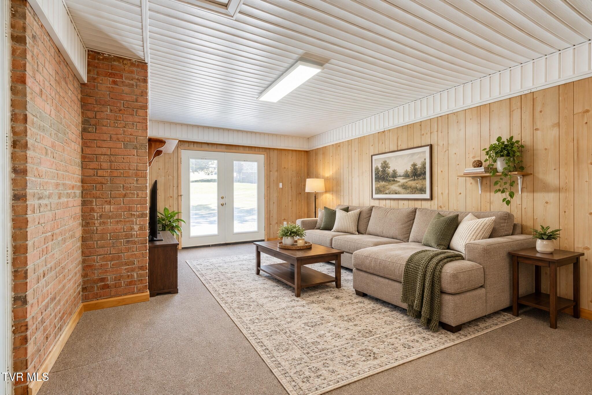 Living room with a beige sectional, wood-paneled walls, exposed brick, and glass double doors.