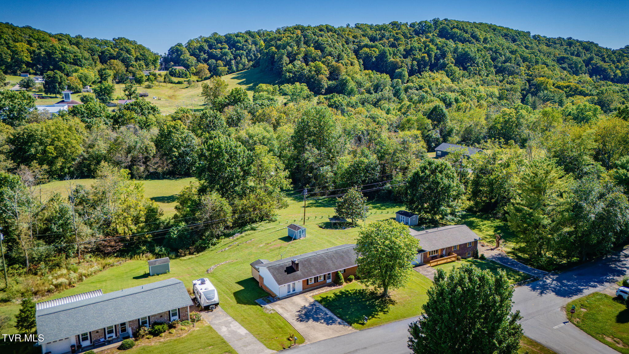 Aerial view of homes and spacious lawns backed by wooded hills.