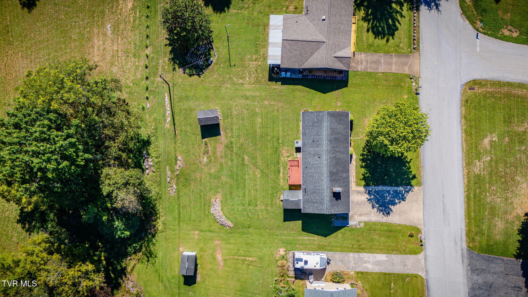 Aerial view of a house and spacious lawn with detached outbuildings beside the road.