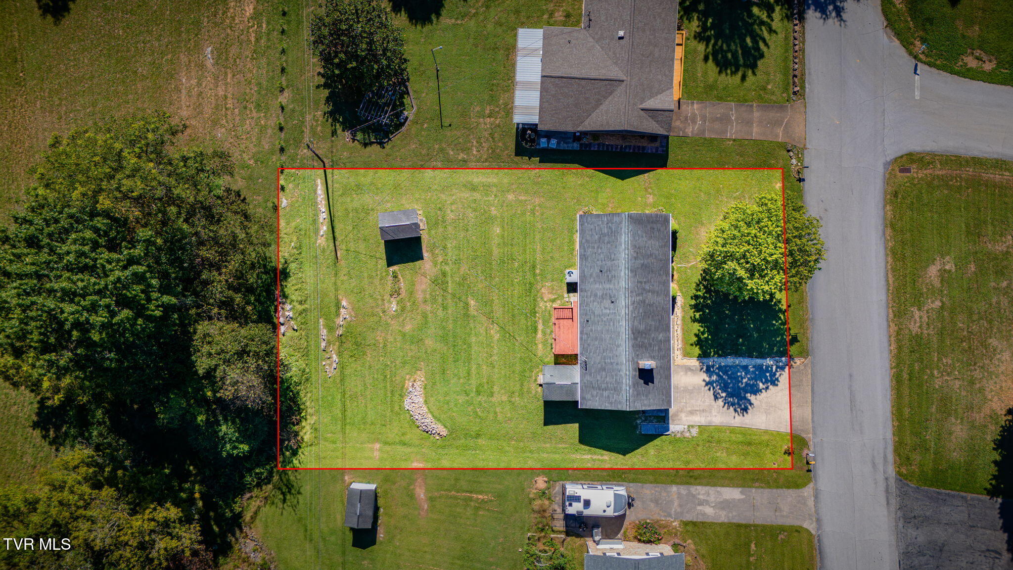 Aerial view of a home and red-outlined lot with a broad lawn and small shed.
