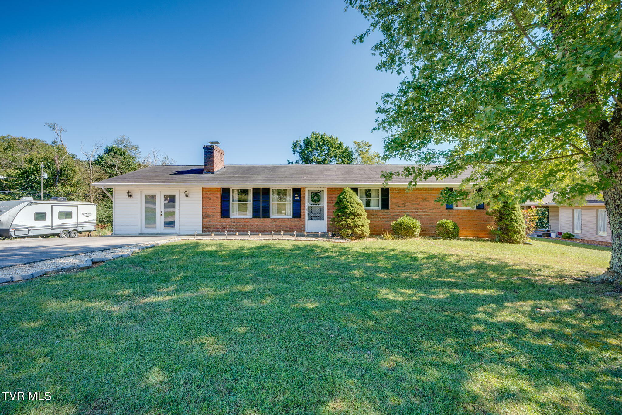 Single-story brick ranch house with a broad lawn, driveway, and large shade tree.