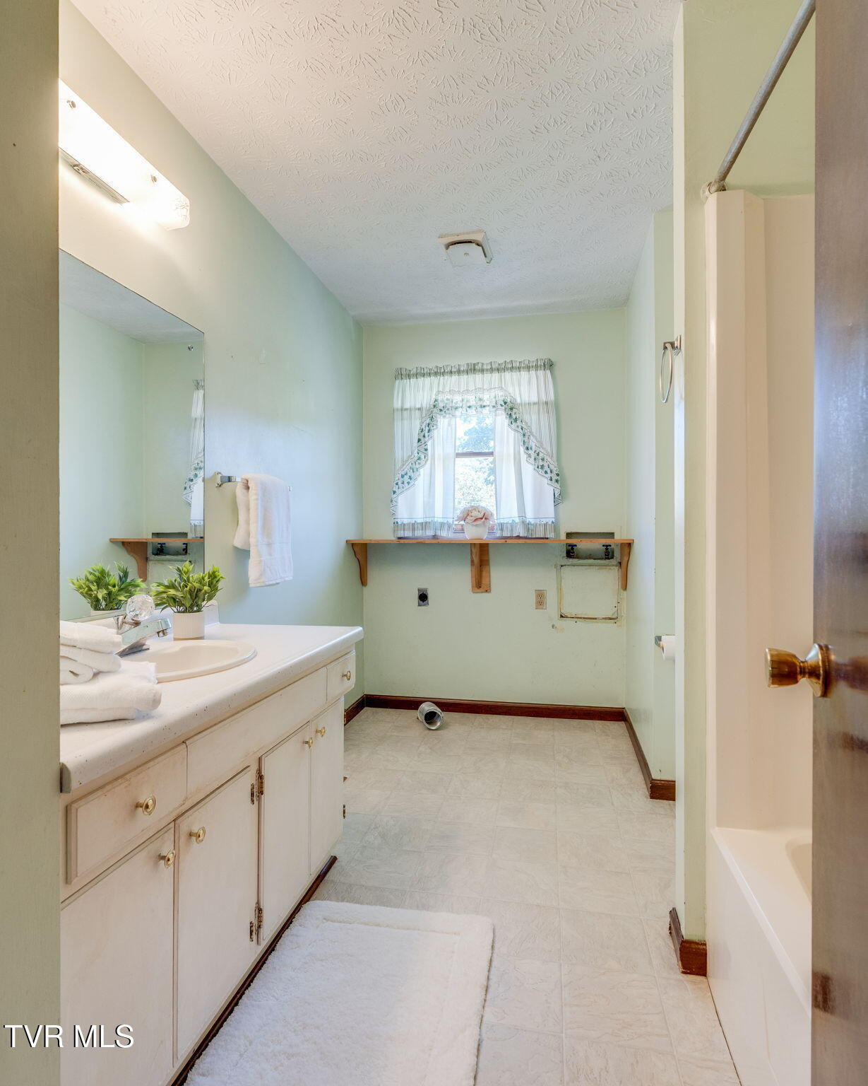 Bathroom with a long white vanity, large mirror, curtained window, and bathtub.