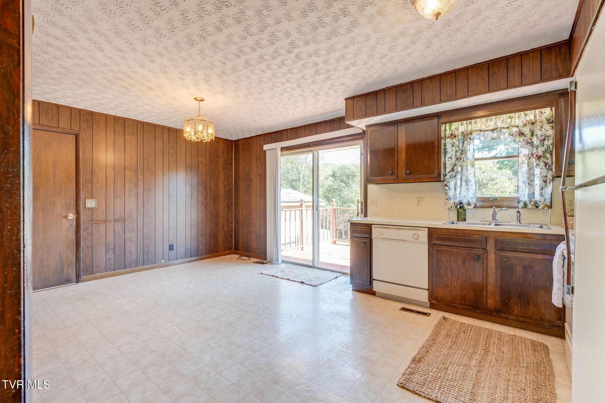 Kitchen with dark wood cabinets and paneling, tile floor, and sliding glass door to a deck.