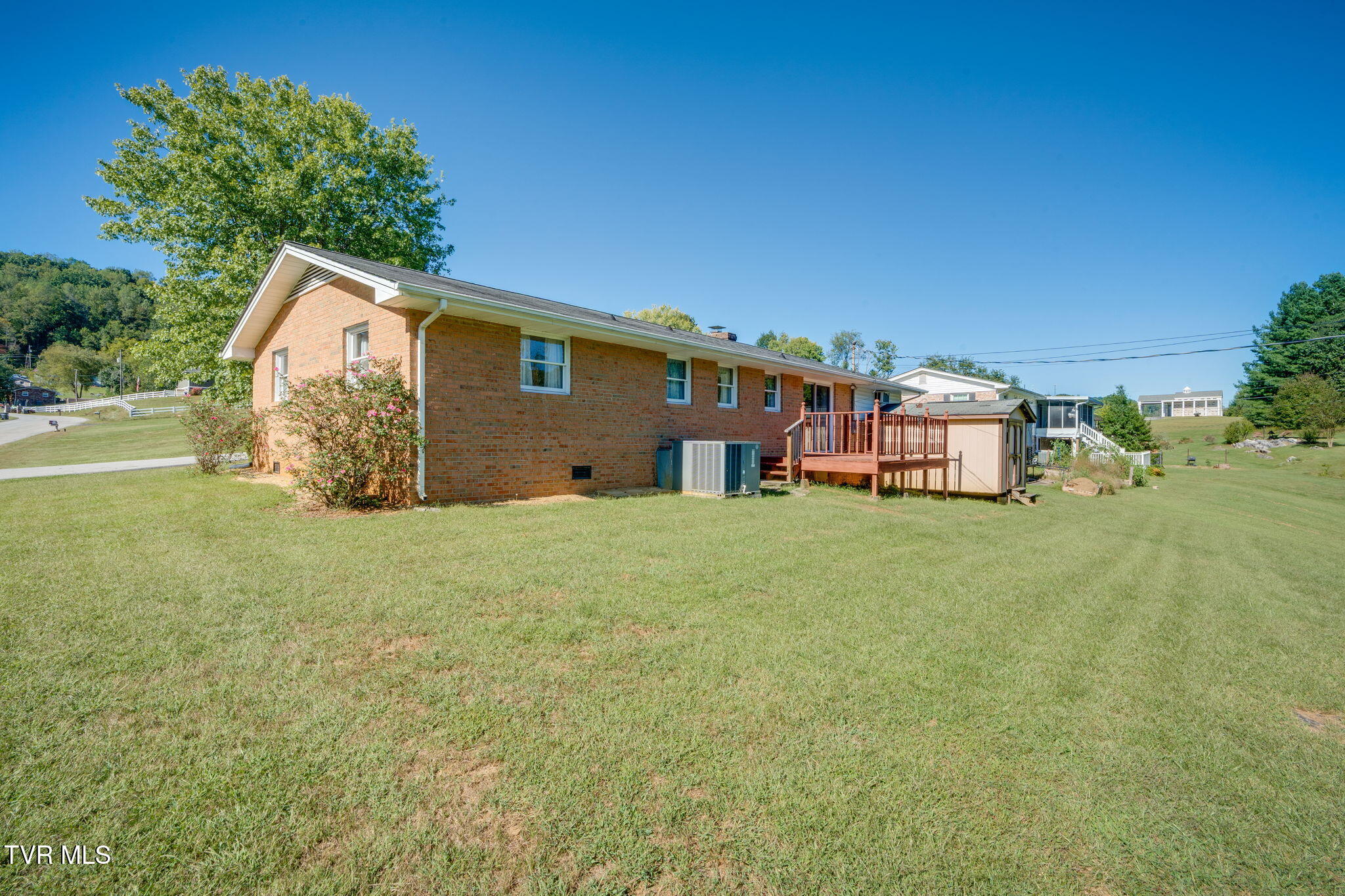Brick house with a raised wooden deck and shed beside a broad grassy yard.
