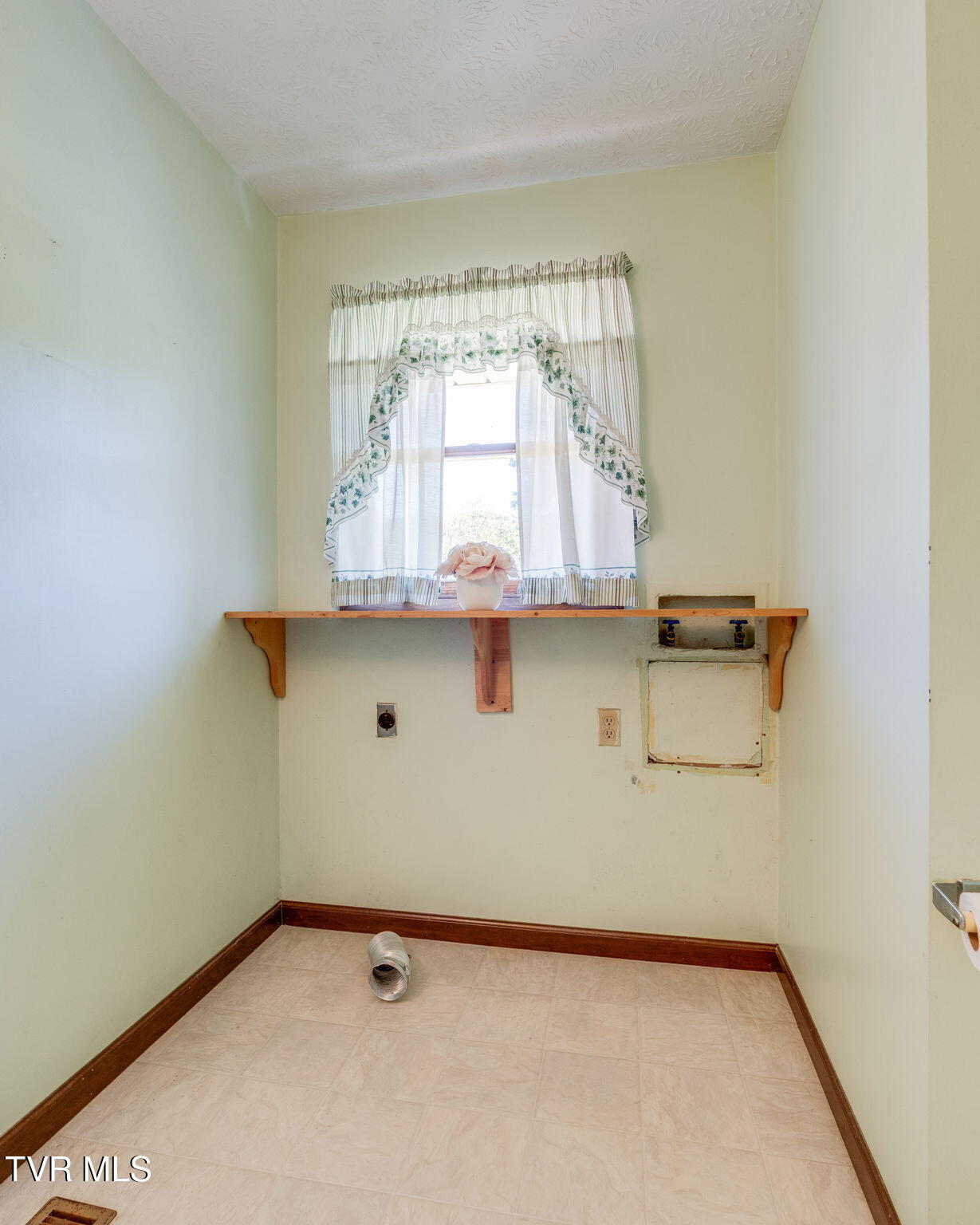Vacant laundry area with washer hookups, a wooden shelf, and a curtained window.