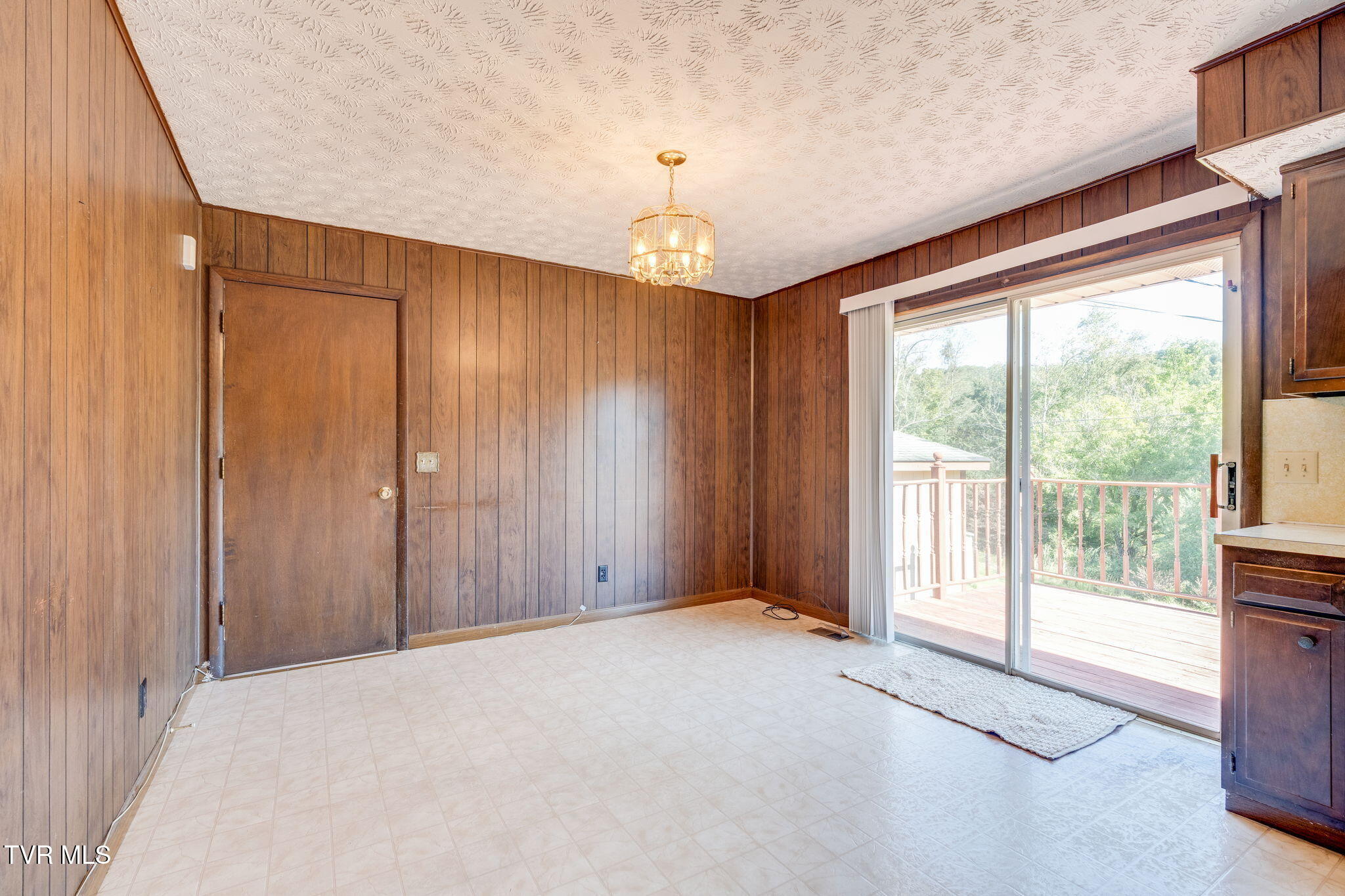 Empty dining area with wood-paneled walls, tiled floor, and sliding glass door to a deck.