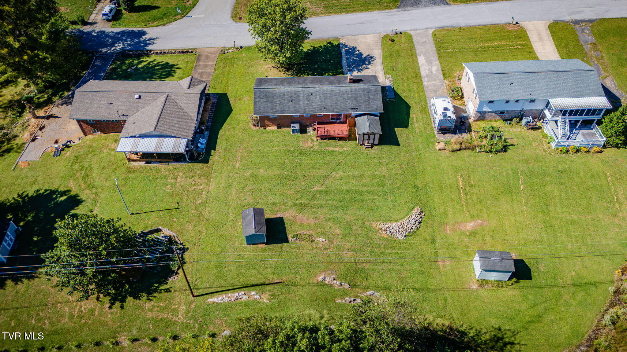 Aerial view of three homes and a broad grassy yard with sheds and driveways.