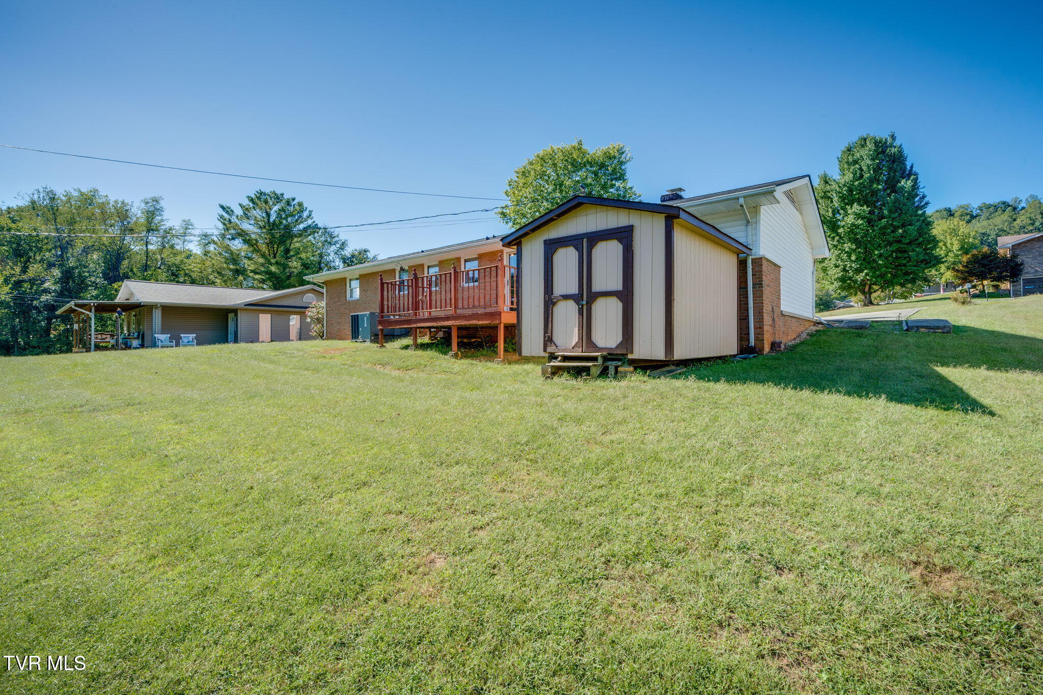 Home with a raised wooden deck and detached shed beside a broad sloping lawn.