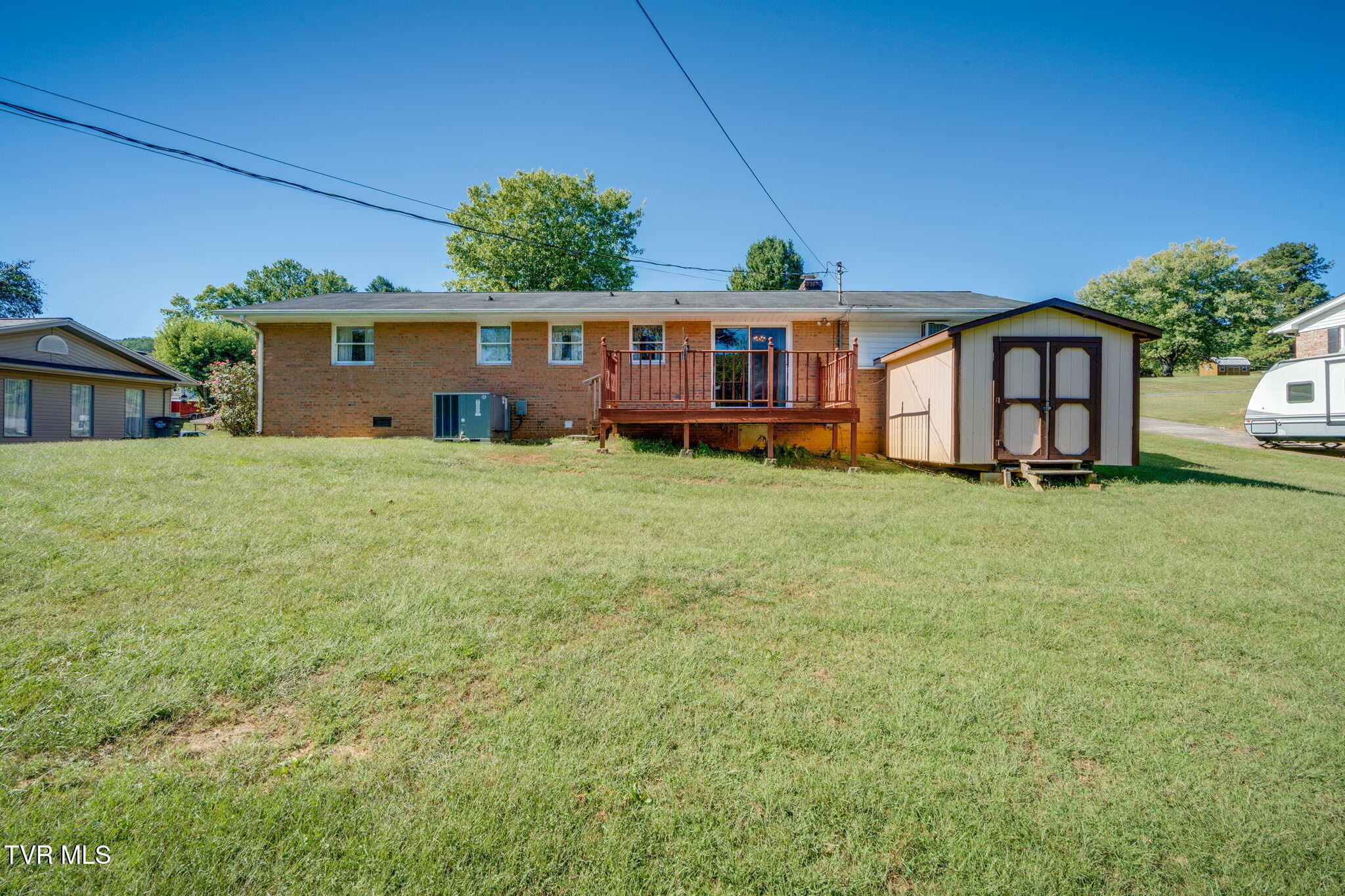 Brick ranch home's rear exterior, raised deck, storage shed, and broad lawn.
