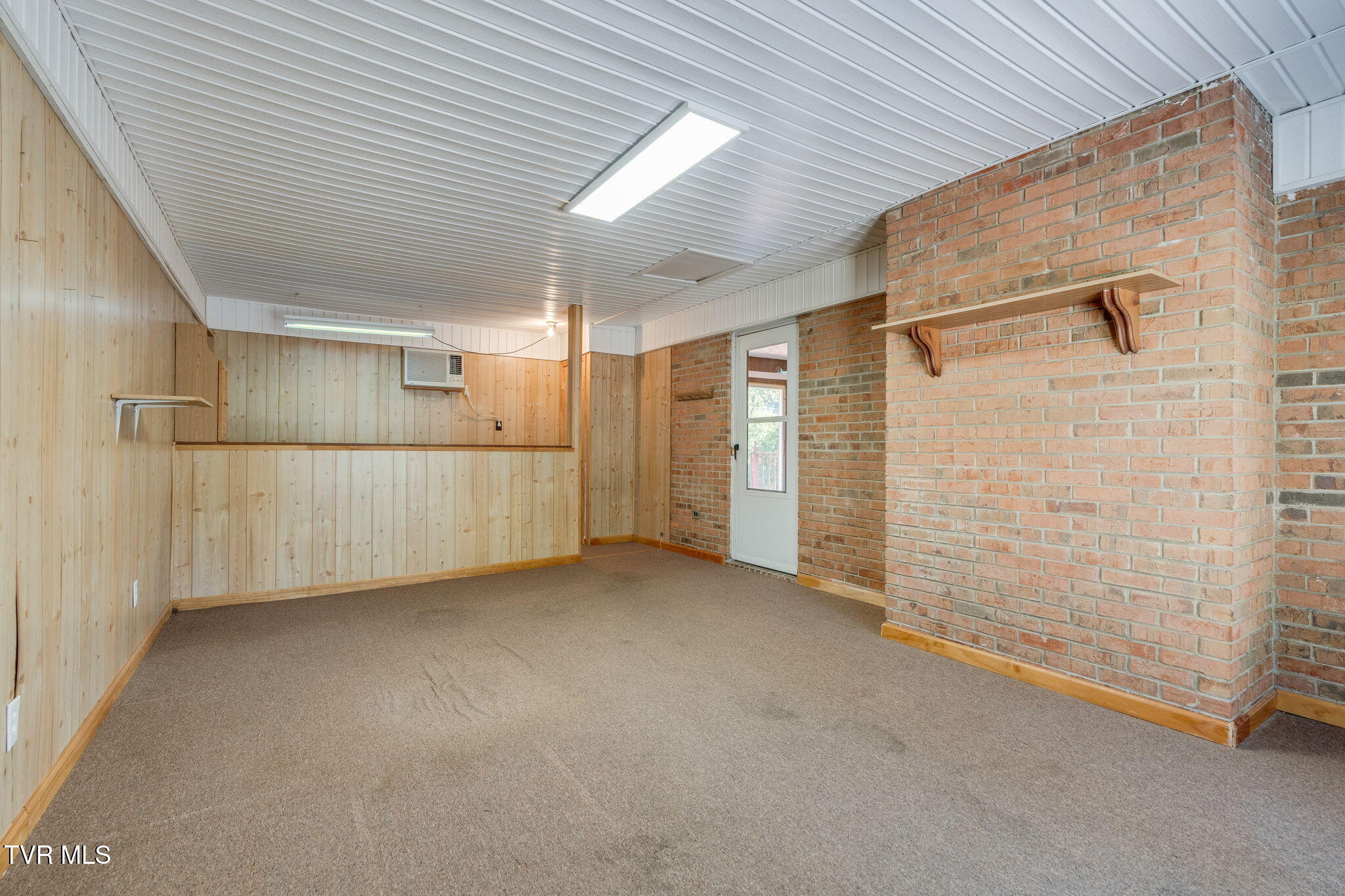 Empty carpeted room with wood-paneled walls and a large brick partition.