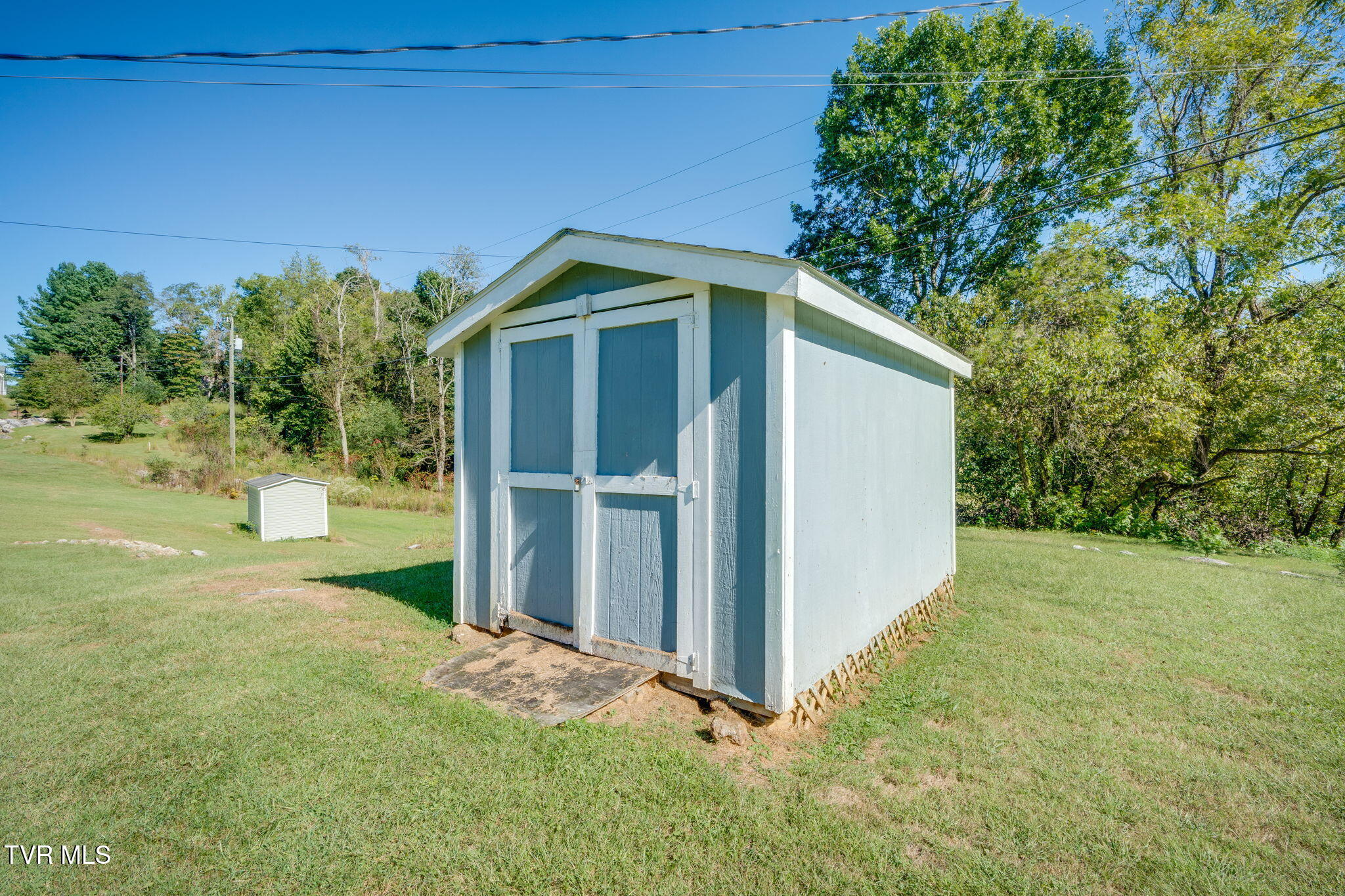 Large light-blue storage shed with white trim and double doors in a grassy yard.