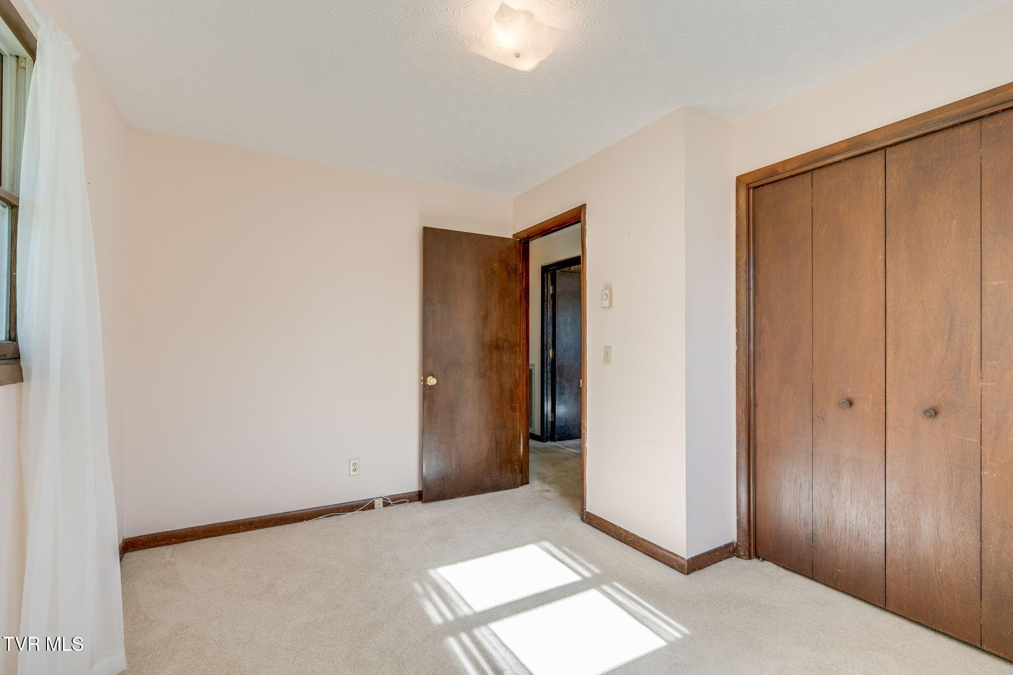 Empty bedroom with a large wooden closet and sunlight falling across the carpet.
