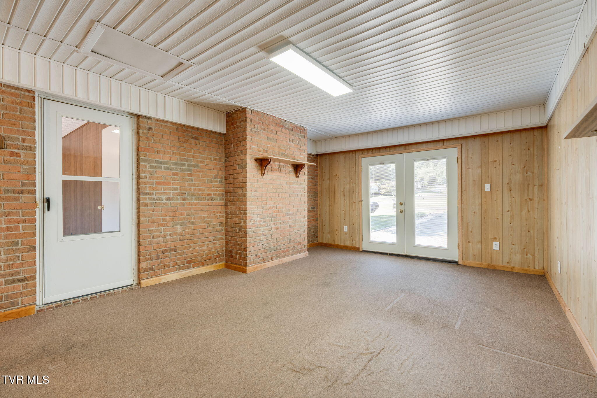 Empty carpeted room with brick walls, wood paneling, and glazed double doors.