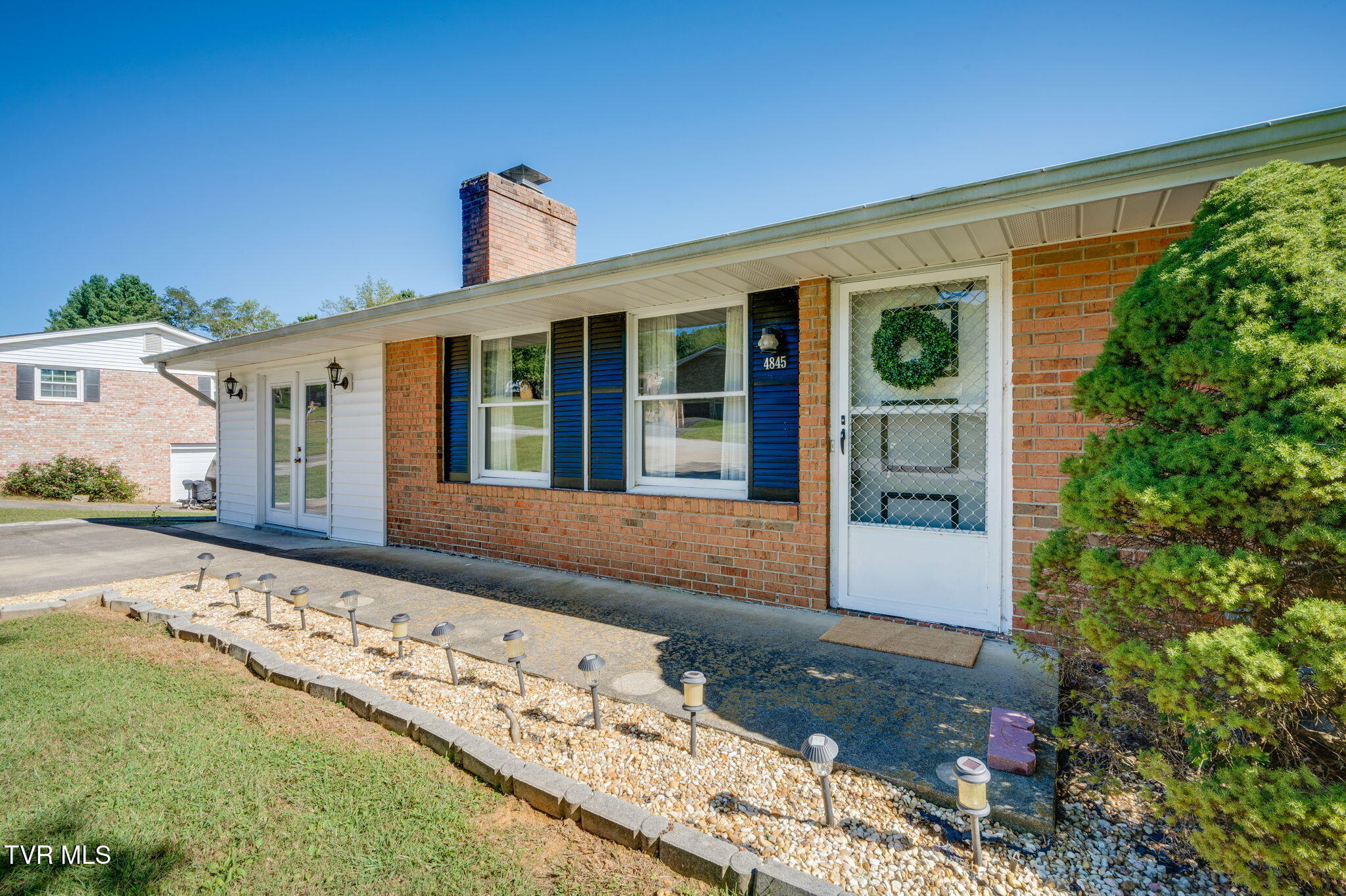 Brick house with blue shutters, a covered entry, and a stone-edged walkway with landscape lights.