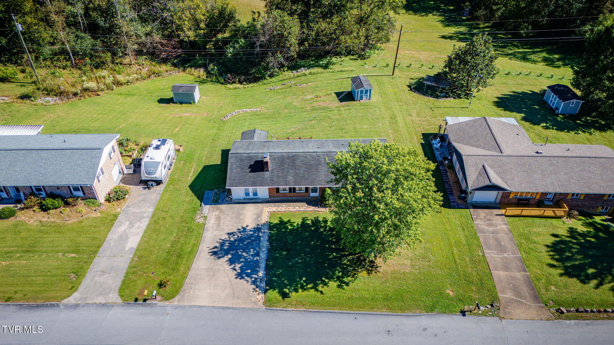 Aerial view of a single-story brick home with a broad grassy backyard and several sheds.