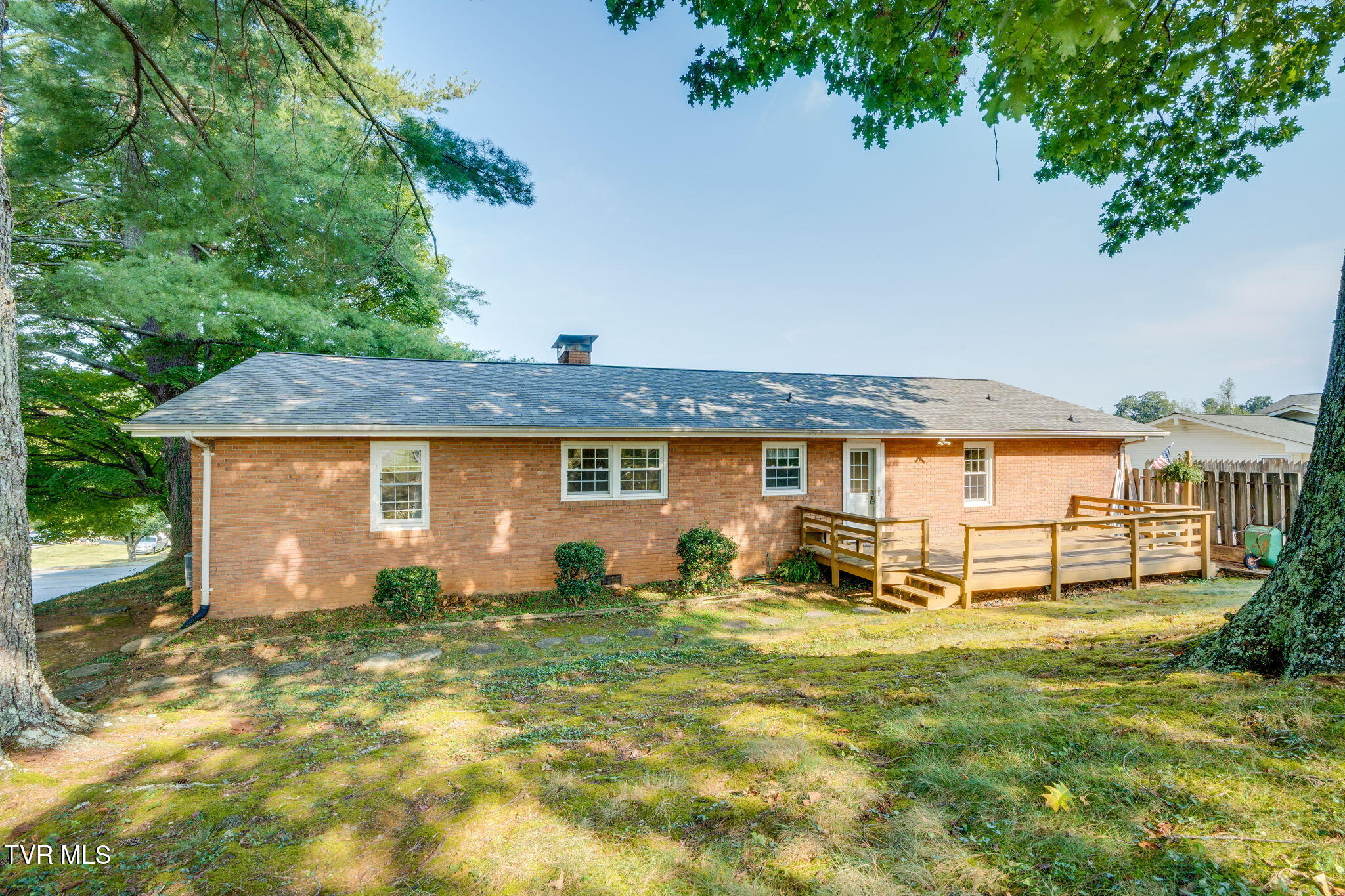 Brick house rear with a raised wooden deck beneath mature trees.