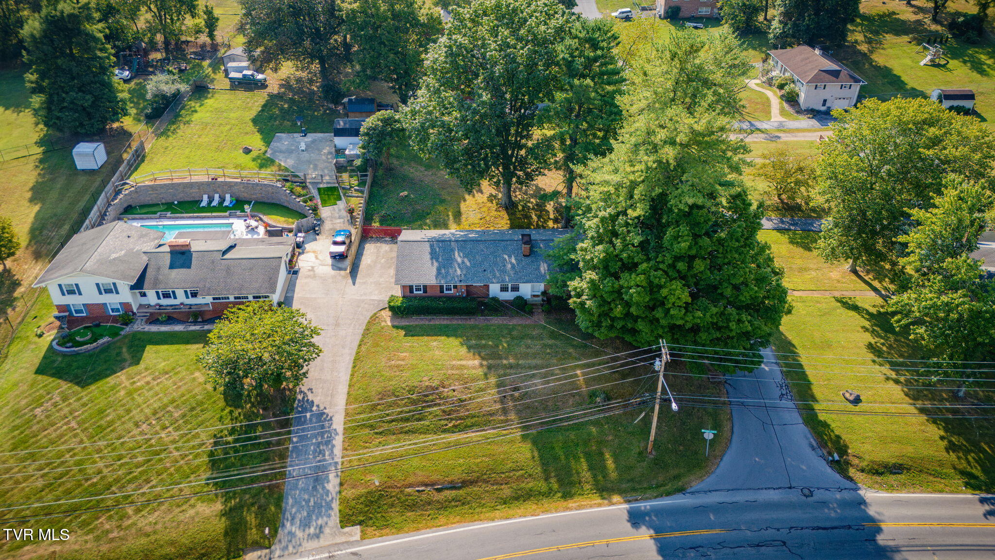 Aerial view of a home with a fenced swimming pool, long driveway, and mature trees.