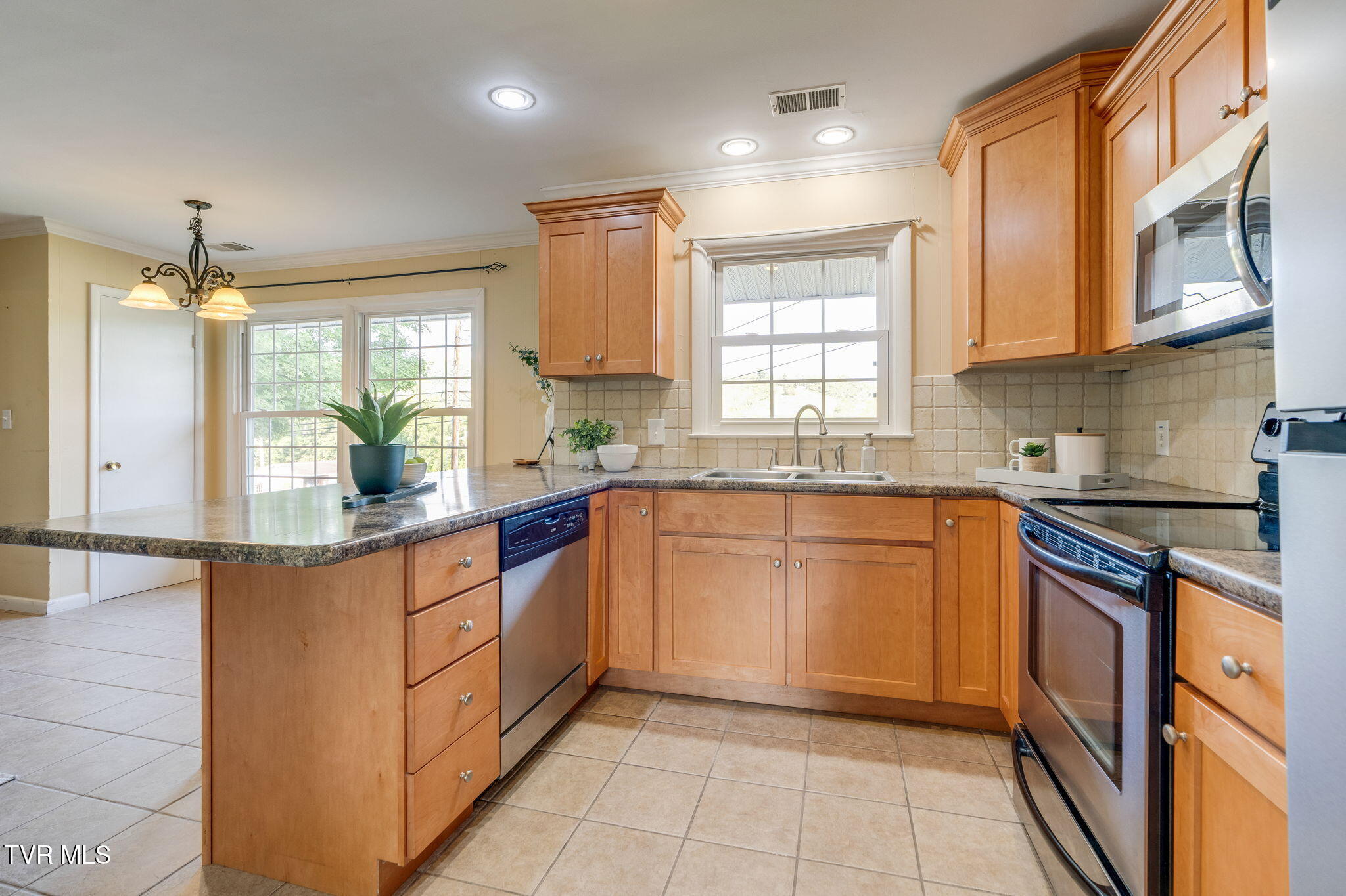 Kitchen with warm wood cabinets, a broad stone peninsula, stainless steel appliances, and a window above the sink.
