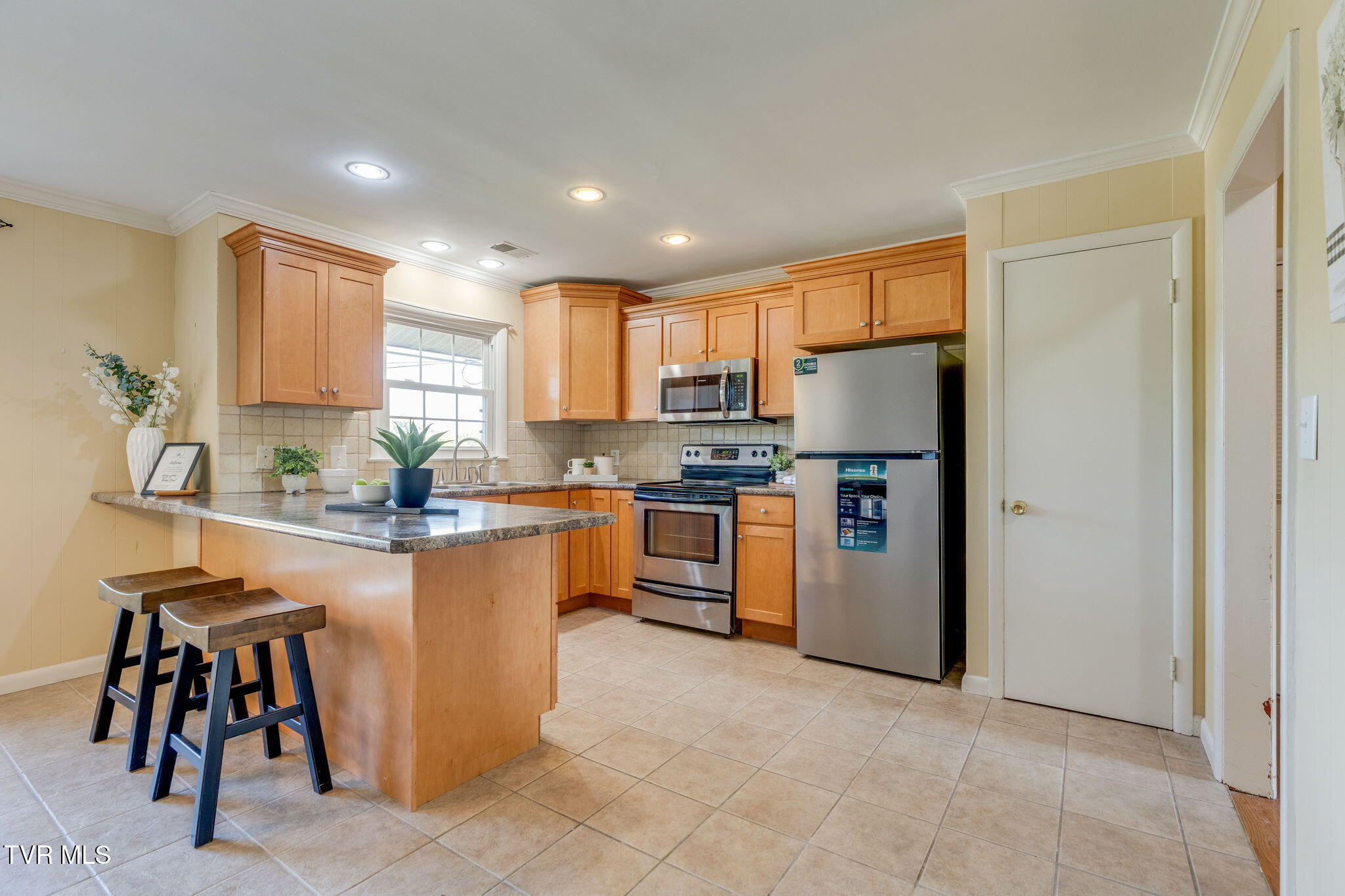 Kitchen with wood cabinetry, stainless steel appliances, and a breakfast island with two stools.