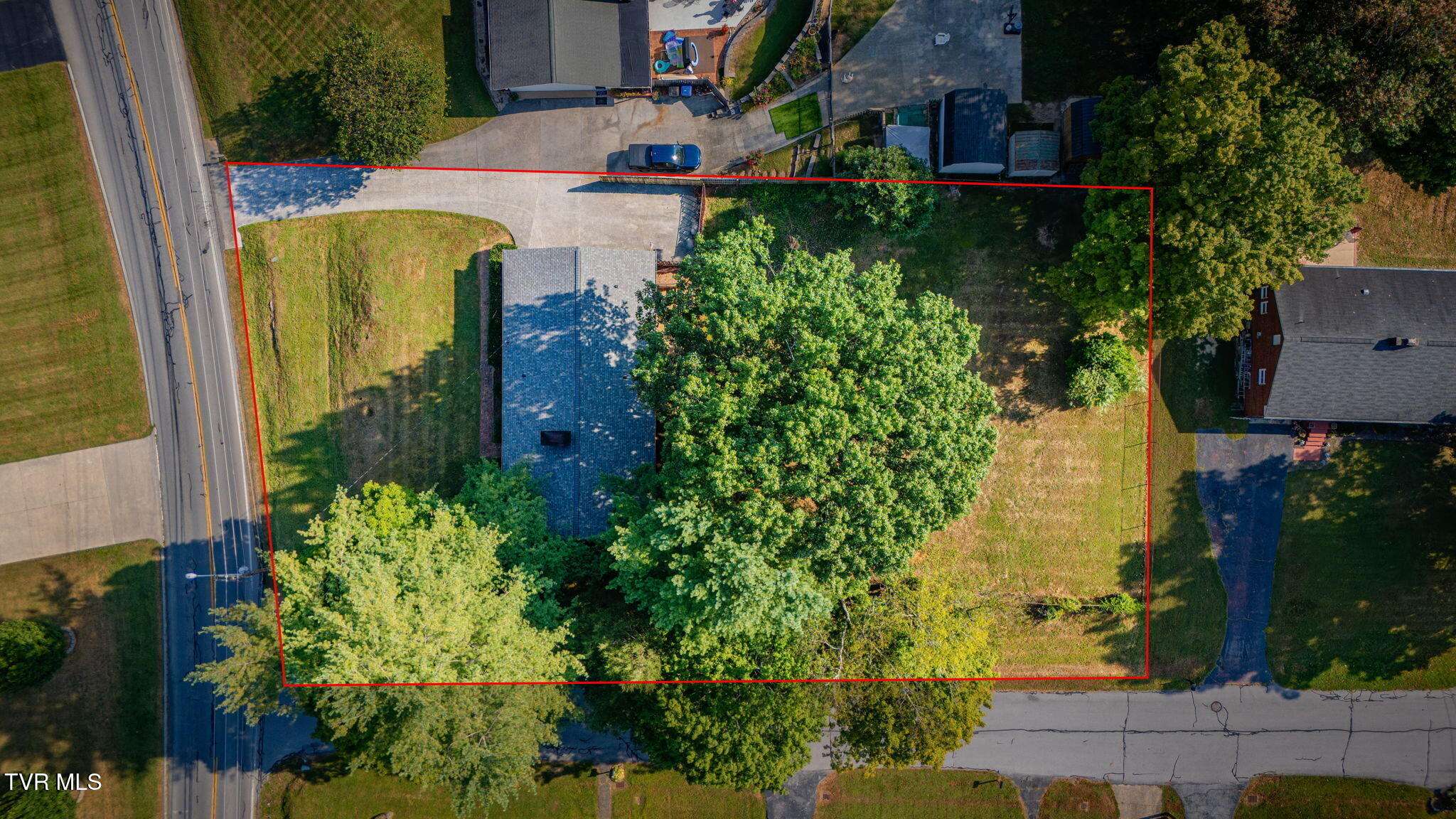 Aerial view of a tree-covered property outlined in red beside a road.